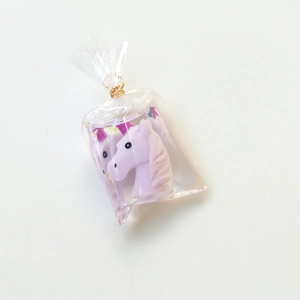 Detail of a purple resin unicorn charm inside a transparent bag with gold metal clasp