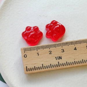 Primer plano de dijes de resina de pata de gato roja con purpurina y escala de medición