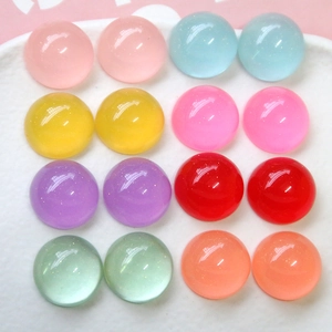 Vue à plat de 16 cabochons en résine pailletée multicolore sur plateau blanc