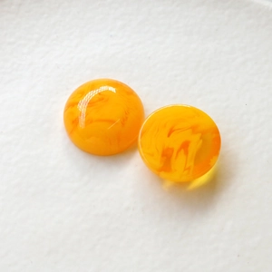 Dettaglio macro di due cabochon in resina arancione marmorizzata per orecchini e gioielli fai da te