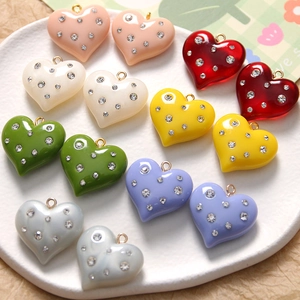 Macro shot of colorful resin heart charms with rhinestones and gold loops on a ceramic plate