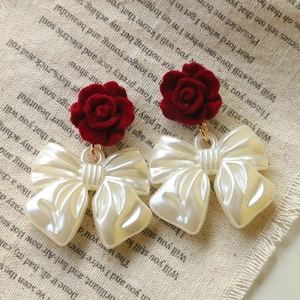 Detailed shot of red velvet rose earrings with pearlescent bow pendants on linen background