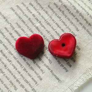 Detailed view of red flocked and resin heart charms on a rustic text-printed fabric
