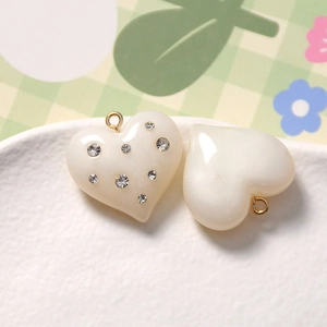 Close-up of resin heart charms with embedded rhinestones and gold loops for DIY jewelry