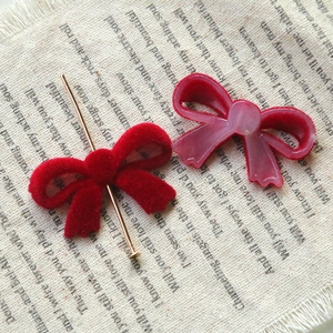 Macro detail of red flocked bow DIY accessory with gold metal pin on vintage burlap background