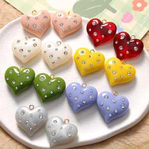 Colorful resin heart pendants with rhinestone accents and gold rings in a ceramic dish