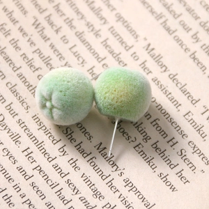 Close-up of green flocked fruit stud earrings with silver pins on a vintage book