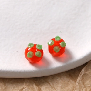 Makroaufnahme roter Glas-Persimone-Perlen mit grünen Blättern für DIY-Schmuck