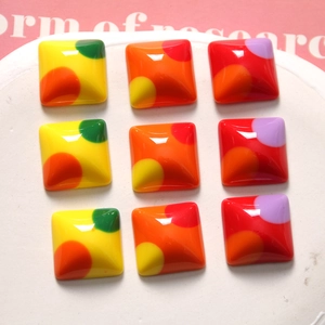 Close-up of nine colorful resin square charms with polka dot patterns for DIY crafts