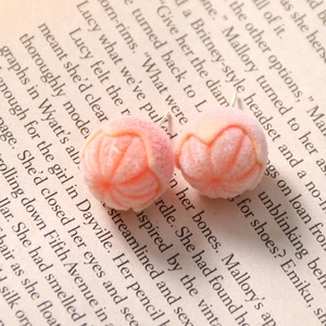 Macro detail of flocked peach stud earrings with green leaves on vintage book pages