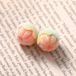 Detail of 3D flocked orange fruit stud earrings on a vintage book page background