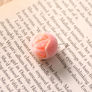 Macro detail of a soft flocked orange fruit stud earring on a vintage book page