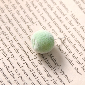 Close-up of a light green flocked spherical earring stud on an artistic book background