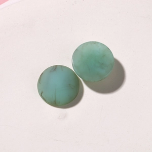 Macro shot of marble textured resin charms with green ink-wash patterns on pink background