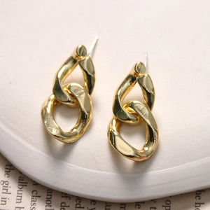 Detailed close-up of retro gold-plated geometric link earrings on a white ceramic tray