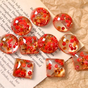 Macro shot of square and round resin DIY charms with embedded red and gold seed beads
