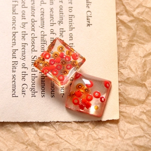 Macro shot of square transparent resin charms with red and orange beads for DIY jewelry