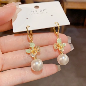Detail of elegant pearl earrings with zircon butterfly and green leaf accents