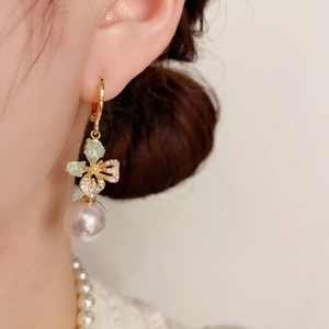 Detail of elegant gold clover earring with green stone, small diamonds and purple pearl