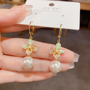 Close-up of elegant gold butterfly and pearl earrings with zircon crystal leaf detail