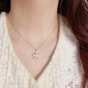Elegant gold chain necklace with white shell flower pendant worn by a model