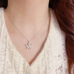 Close-up of a delicate silver flower pendant necklace with white shell petals on a woman