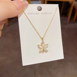 Detailed close-up of a golden maple leaf pendant necklace with white shell inlay