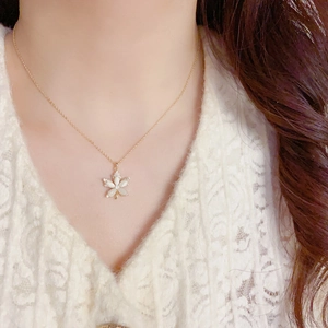 Detailed close-up of golden maple leaf pendant necklace with white shell inlay and crystals