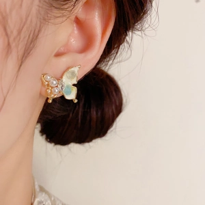 Orecchini a farfalla dorati con perle bianche e dettagli blu su modella per stile chic