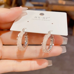 Detalle de pendientes de aro plateados con cristales brillantes en tarjeta joya