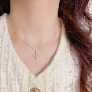 Gros plan du collier croix dorée avec zircons en forme de poire sur le décolleté