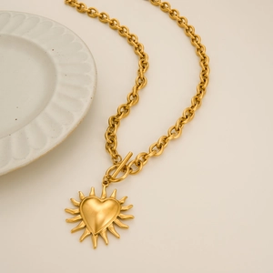 Dettaglio della collana con ciondolo a cuore sole in oro 18k e chiusura a T su un piatto