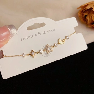 Elegant gold celestial bracelet with sparkling star and moon charms on a fashion display card