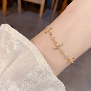 Elegant gold-plated cross bracelet with sparkling zircons worn over white lace cuff