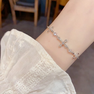 Silver cross bracelet with inset crystals worn on wrist with white lace sleeves