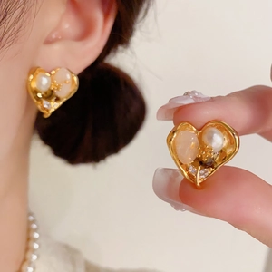 Détail de boucles d'oreilles cœur avec perles et pierres sur monture dorée