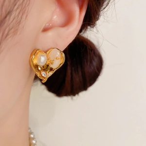 Gros plan sur la boucle d'oreille cœur en or avec perle blanche et détail de fleur