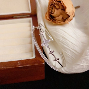 Elegant silver open bangle with double-layer cubic zirconia clover next to a rose