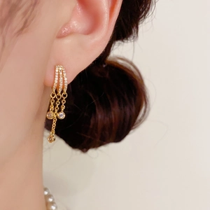 Detalle de pendientes de borla dorados de lujo con circonitas en una modelo femenina