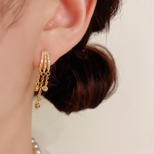 Detalle de pendientes de lujo con borlas doradas, pavé de circonitas y cadenas colgantes