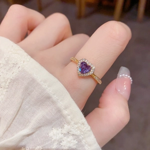 Détail de la bague dorée ornée d'une pierre coeur violette et de diamants scintillants