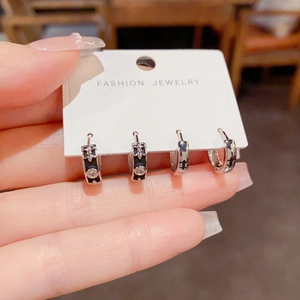 Detail van zilveren oorbellen met kruis en ster, zwart emaille en heldere strassteentjes