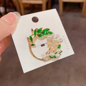 Elegant gold flower brooch with green enamel leaves and white pearls on display card