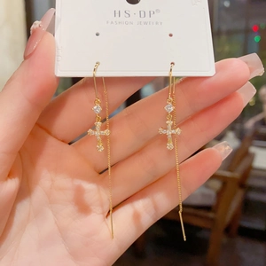 Détail de boucles d'oreilles traversantes croix dorée avec zircons brillants sur carte