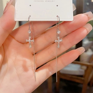 Détail de boucles d'oreilles croix en argent avec pompons en zircone sur une carte