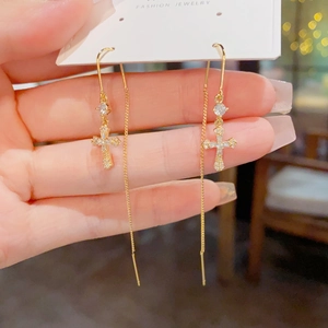 Détail des boucles d'oreilles pendantes dorées avec croix en zircon sur un carton