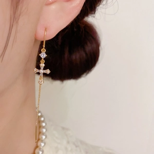 Gros plan de boucles d'oreilles croix dorées à pampilles avec zircons étincelants