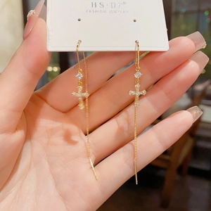 Détail des boucles d'oreilles croix dorées avec zircones cubiques et chaîne longue