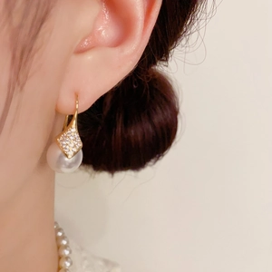 Detalle de pendiente de perla con rombo de circón y elegante gancho dorado