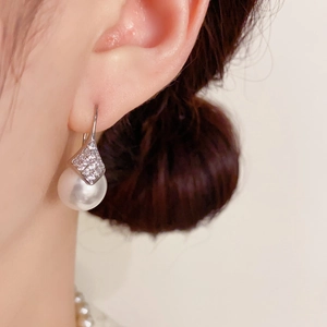 Detalle de los pendientes de perlas con rombos de diamantes puestos en la oreja